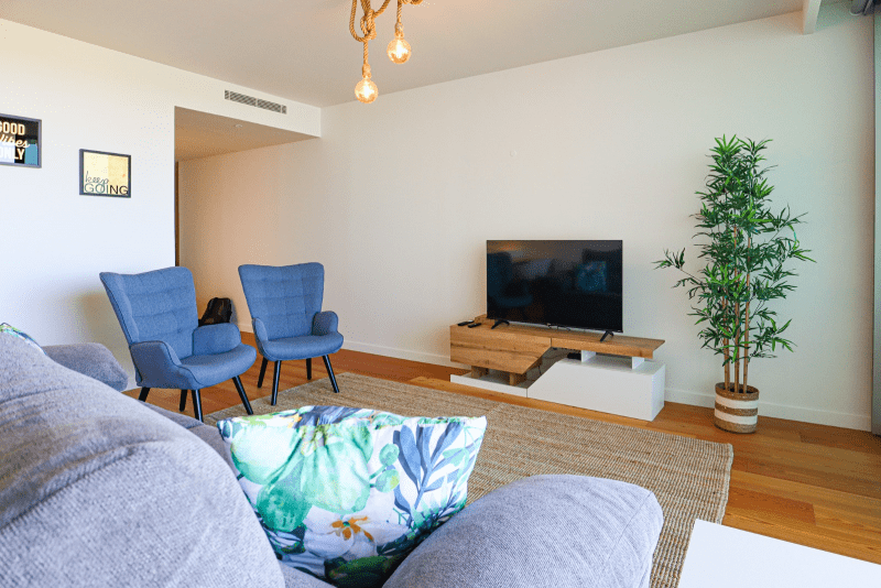 Salmão living room at Bayline, Armação de Pêra: grey sofa with tropical cushion, blue armchairs and TV