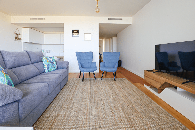 Salmão living room at Bayline, Armação de Pêra: grey sofa, blue armchairs and TV, with the kitchen behind