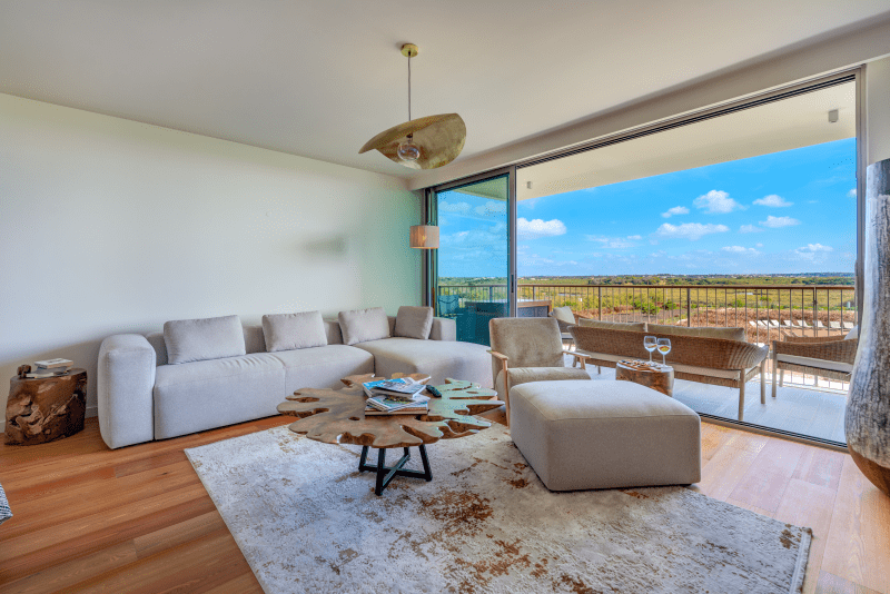 Raia living room at Bayline, Armação de Pêra: white sofa, ottoman and glass doors to the balcony with open views