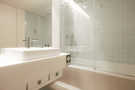 Bacalhau bathroom at Bayline, Armação de Pêra: basin and glass-screened bathtub with shower