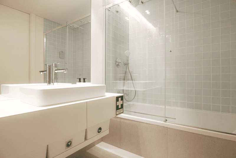 Bacalhau bathroom at Bayline, Armação de Pêra: basin and glass-screened bathtub with shower