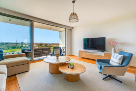 Enguia living room at Bayline, Armação de Pêra: sofa, blue armchair, round coffee tables and glass doors to the balcony