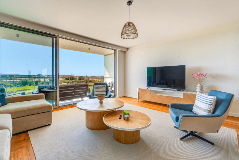 Enguia living room at Bayline, Armação de Pêra: sofa, blue armchair, round coffee tables and glass doors to the balcony