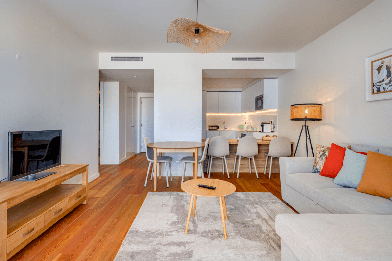 Corvina living room at Bayline, Armação de Pêra: sofa, TV unit and round coffee table, dining area and kitchen behind