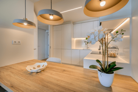 Liro kitchen at Bayline, Armação de Pêra: wooden breakfast bar with orchid under pendant lights, white kitchen behind