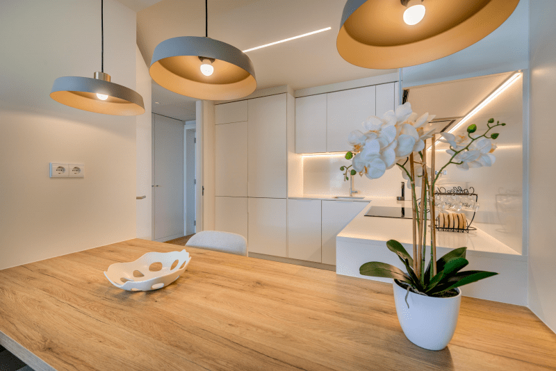 Liro kitchen at Bayline, Armação de Pêra: wooden breakfast bar with orchid under pendant lights, white kitchen behind