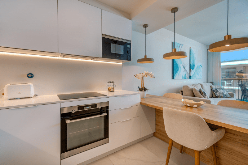 Liro kitchen at Bayline, Armação de Pêra: built-in oven, microwave and induction hob, breakfast bar and living room beyond