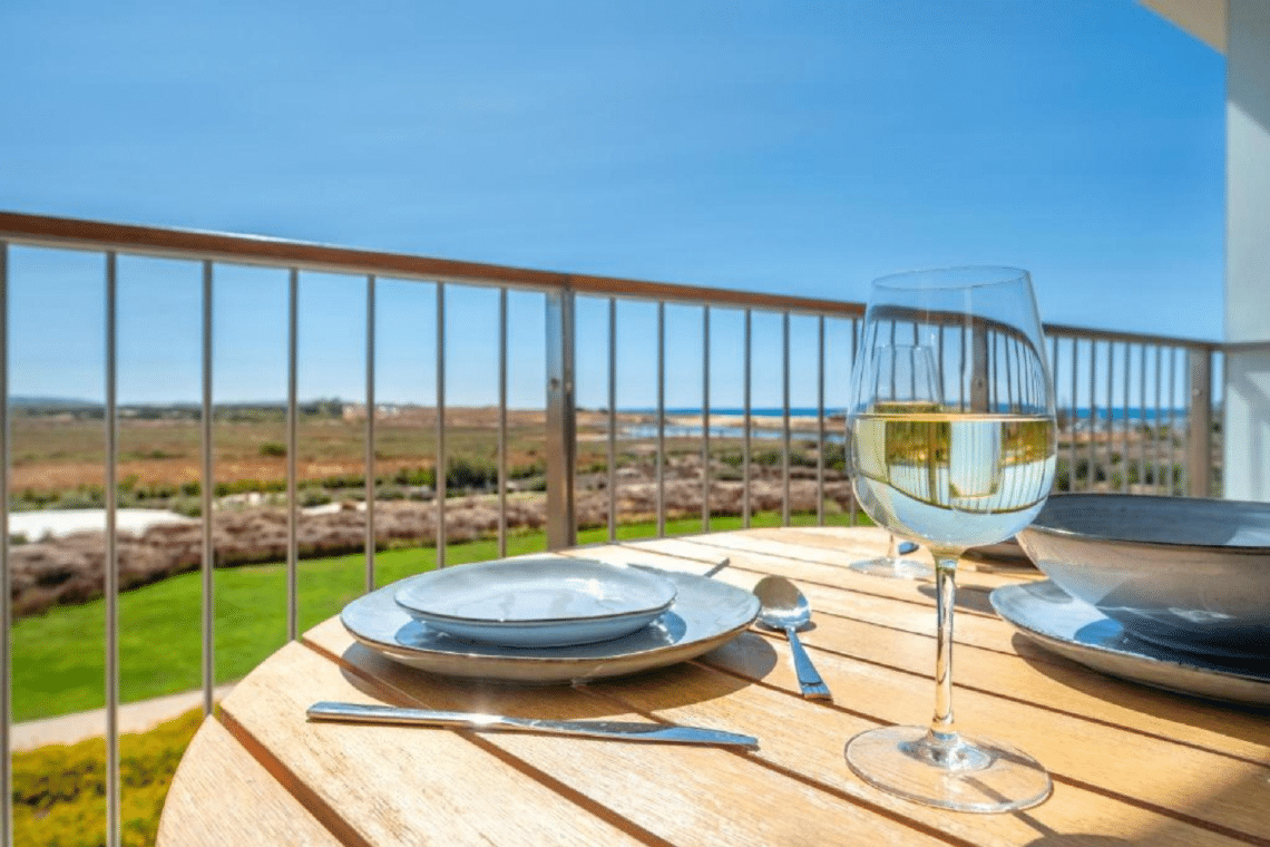 Nemo balcony at Bayline, Armação de Pêra: table laid with a glass of white wine, gardens and lagoon beyond